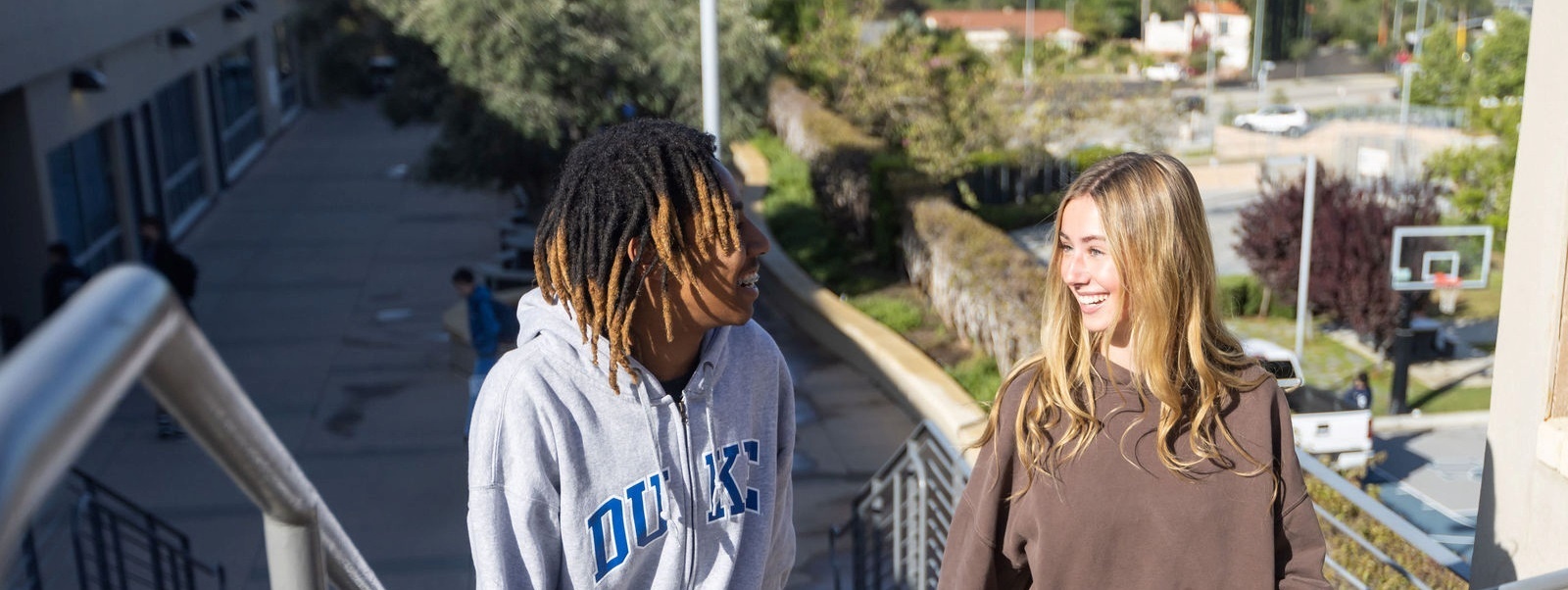 Smiling Sierra Canyon students, a boy and a girl, happily walking down a flight of stairs.