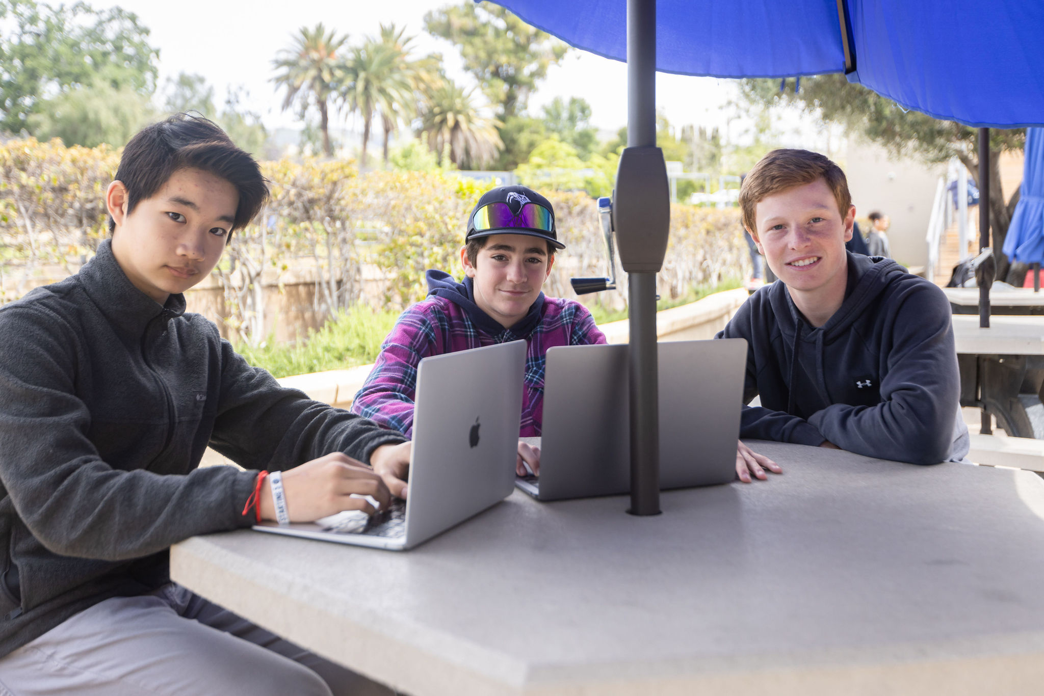 Middle School students sitting at a table outside with computers collaborating on Sierra Canyon academics.