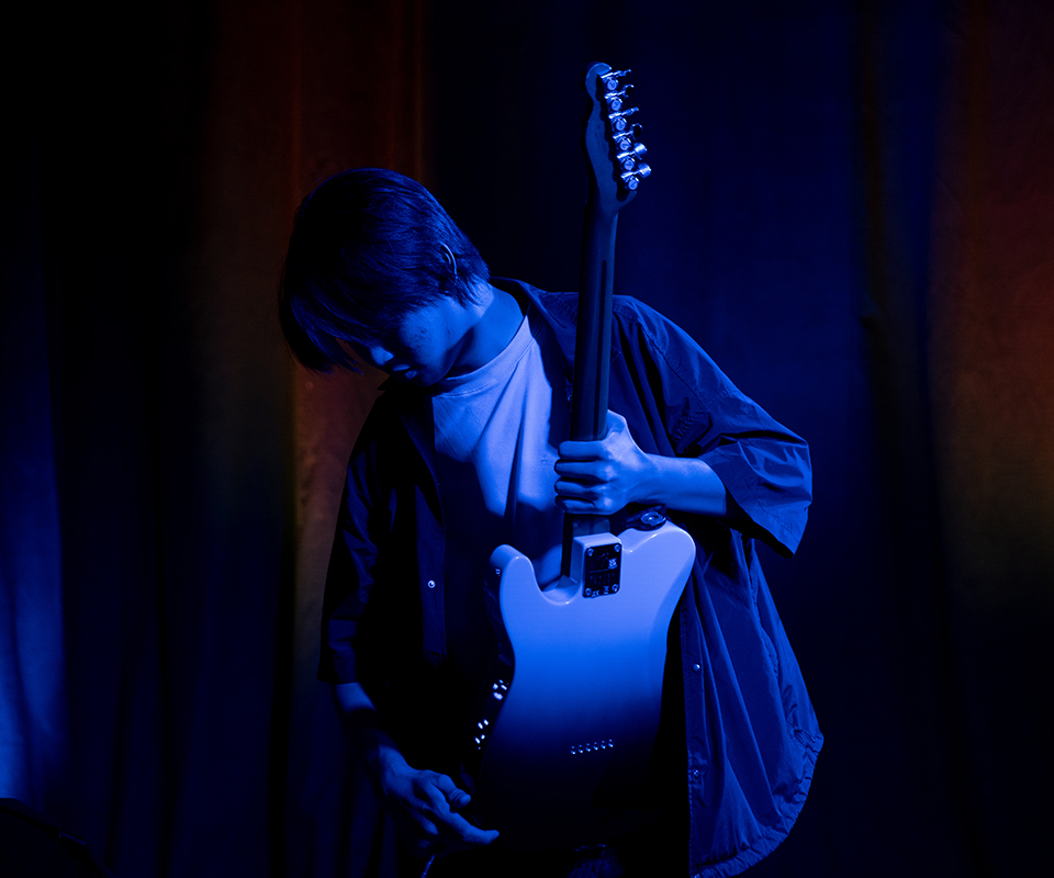 A picture of a male student picking up his guitar for a performance