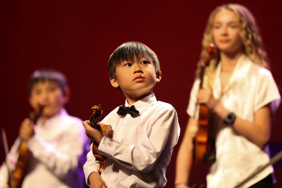Boy performing violin in front of audience at Sierra Canyon arts program.